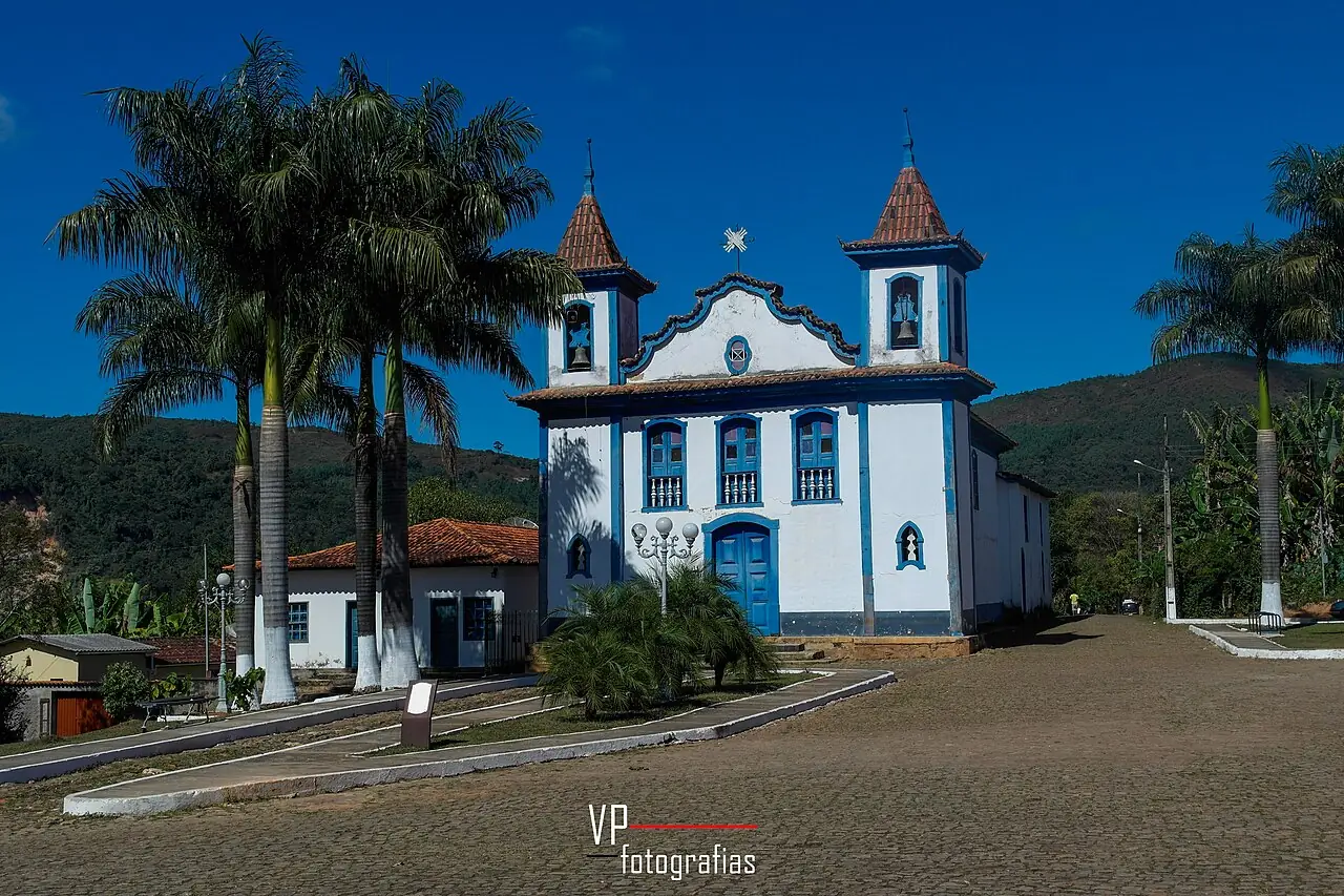 Igreja histórica de fachada branca com detalhes azuis e duas torres, no largo de calçamento de pedra de Cocais, em Barão de Cocais (MG)